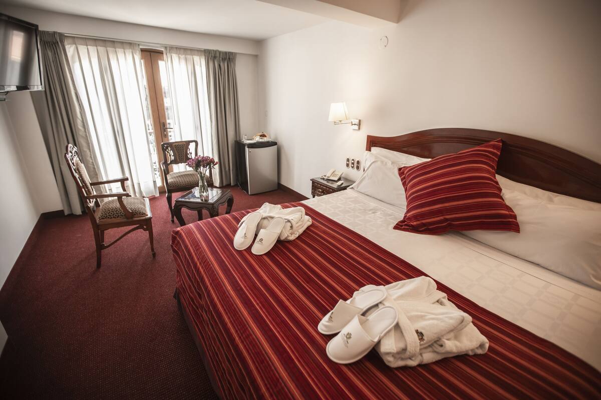 A hotel room with a bed, a chair, a desk, a lamp, and a TV.