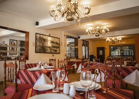Un restaurante con varias mesas dispuestas para comensales, que cuenta con una araña y un cuadro grande en la pared.