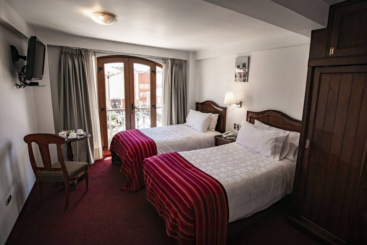 A hotel room with two beds, a desk with a chair, a TV, and a wardrobe.