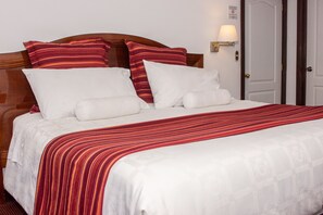 A neatly made bed with a striped red and white bedspread, white pillows, and a wooden headboard. - Hacienda Plaza de Armas (Puno)