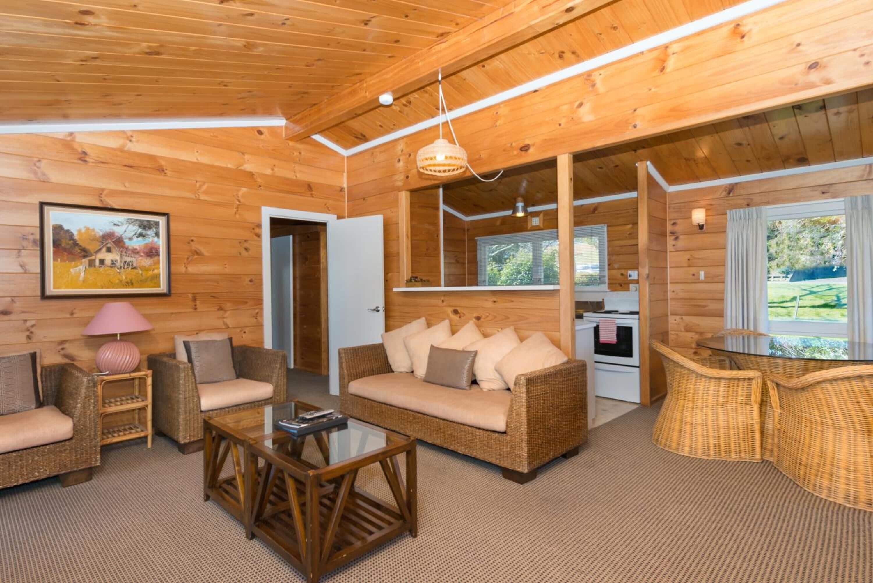 L'intérieur d'un chalet en bois comprend un canapé, une table basse, des fauteuils en osier, une table à manger et un coin cuisine.