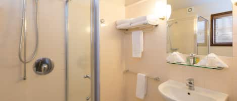 A bathroom with a glass-enclosed shower, a white sink, and a mirror with a glass shelf above it.