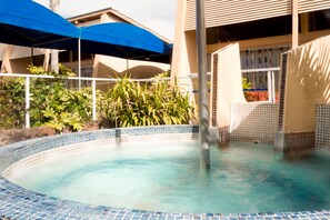 A swimming pool with a tiled edge, surrounded by plants and a building with a balcony. - Oasis Beach Motel  (Taupo)