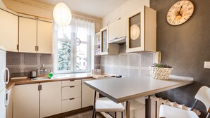 A modern kitchen with white cabinets, a dining table, and a clock on the wall. - The Secret Garden Apartments (Kraków)
