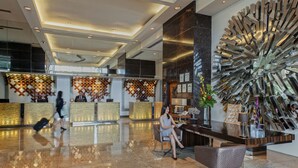 A modern lobby with a reception desk, seating area, and decorative wall art. - Acacia Hotel Manila (Muntinlupa)