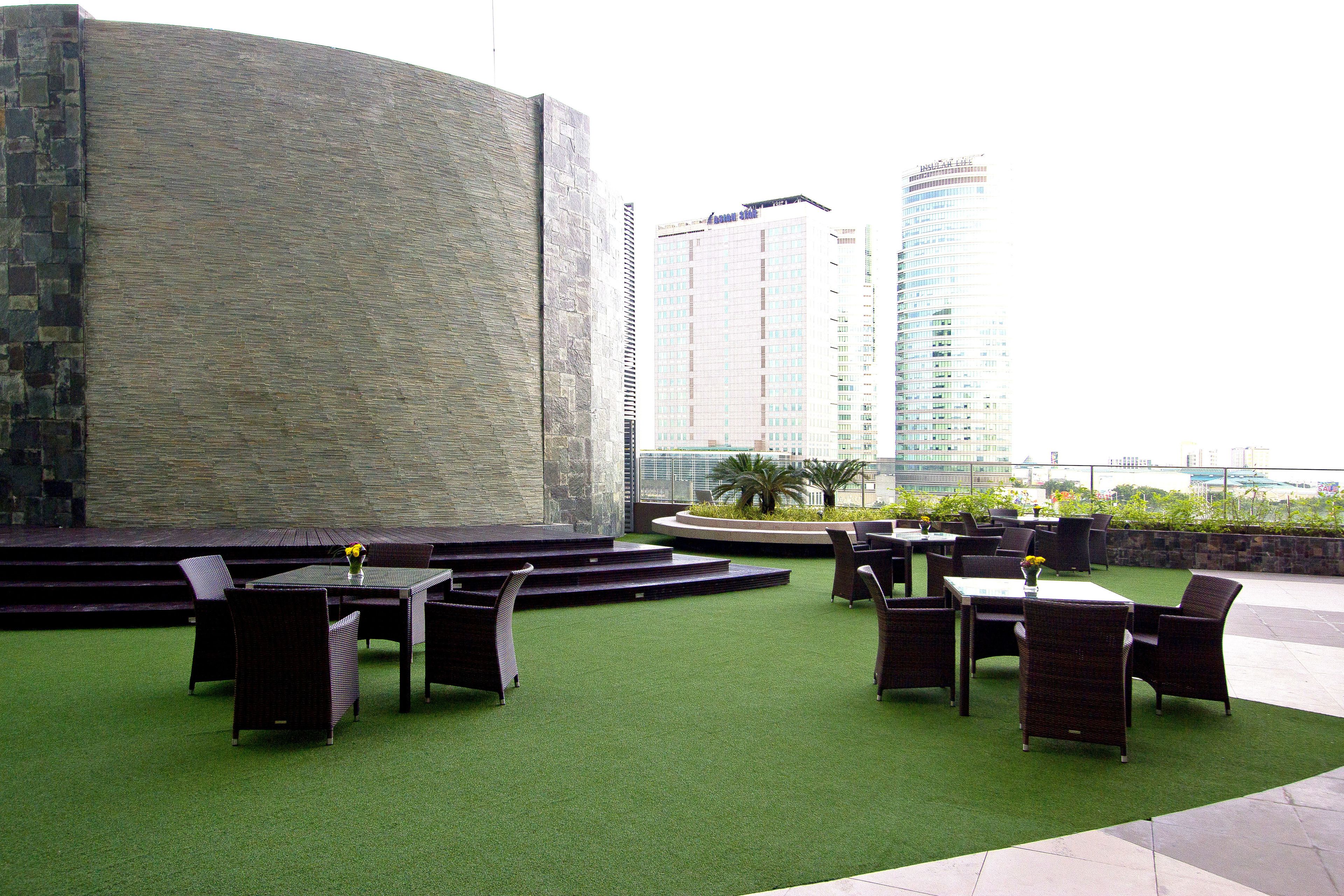 Un área de estar al aire libre con césped artificial, mobiliario de mimbre y una pared de piedra.