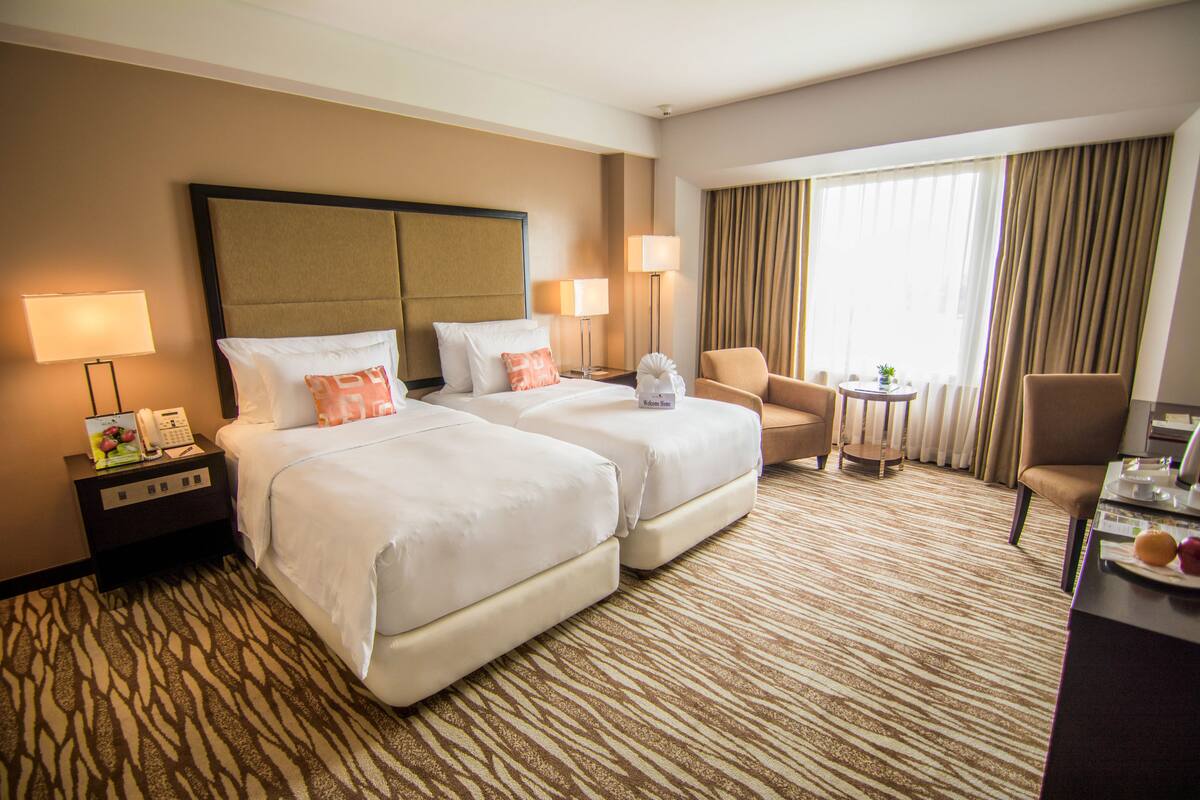 A hotel room with two beds, a desk, a chair, a small table, and a window with curtains.