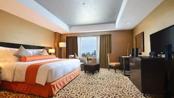 A hotel room with a large bed, a desk, a chair, a television, and a view of the city.