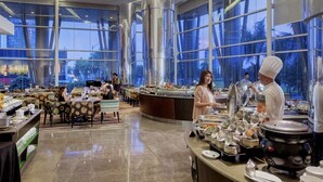 A spacious buffet area with multiple serving stations, a central counter, and a seating area with tables and chairs. - Acacia Hotel Manila (Muntinlupa)