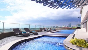 A rooftop pool with lounge chairs and a city view. - Acacia Hotel Manila (Muntinlupa)