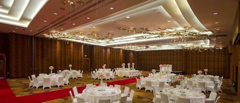 A banquet hall with round tables, white chairs, and red carpet.