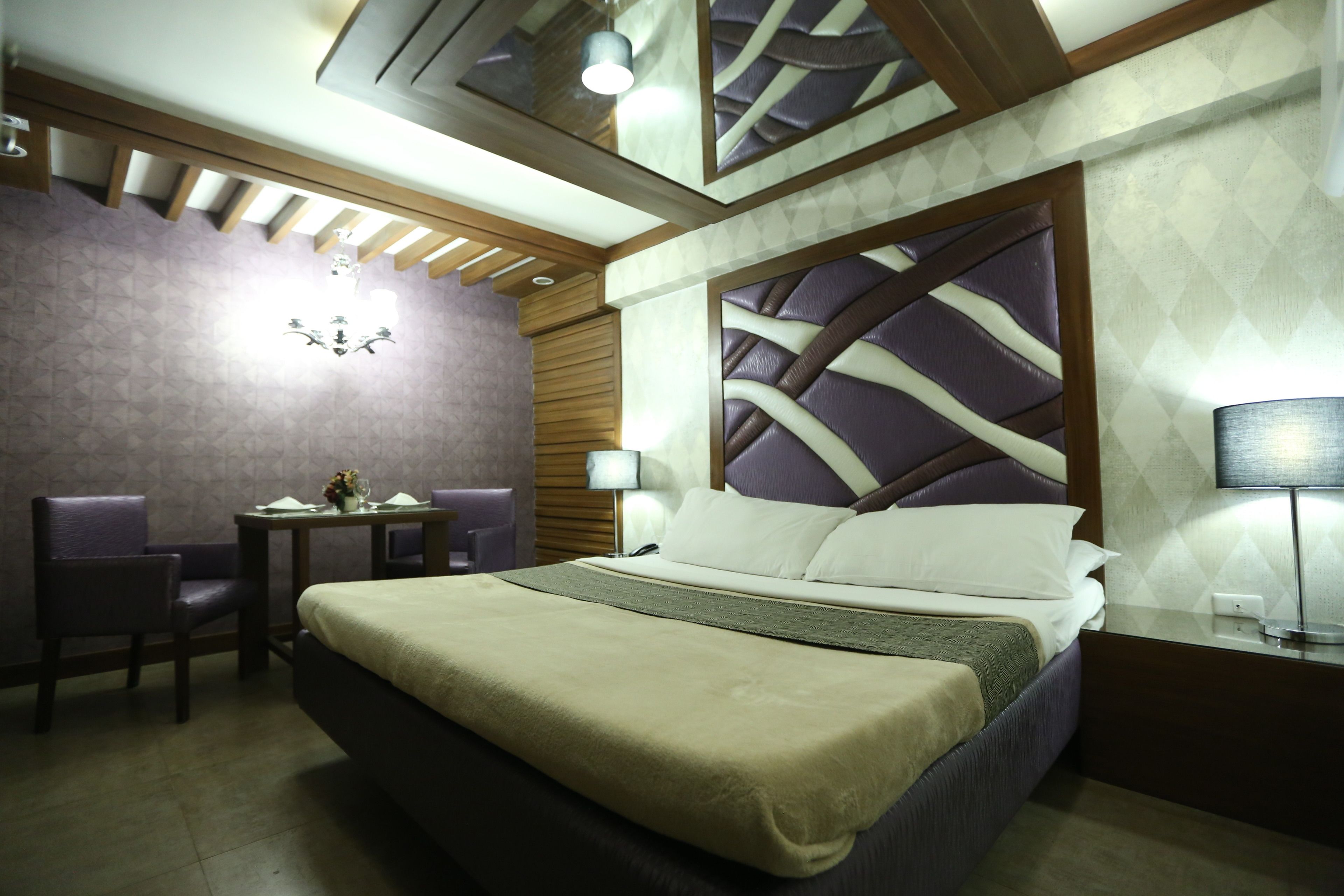 A hotel room with a large bed, a desk with a chair, a small table with a vase, and a nightstand with a lamp.