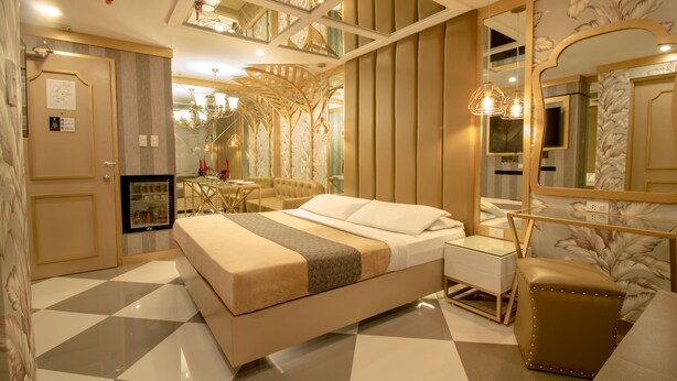 A modern hotel room with a large bed, a small desk, a vanity, and a mirror. - Victoria Court Hillcrest - Pasig (Pasig)
