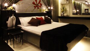 A modern bedroom with a large bed, a nightstand, a mirror, and a decorative wall with floral patterns. - Victoria Court Hillcrest - Pasig (Pasig)