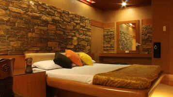 A bedroom with a stone wall, a bed with multiple pillows, a wooden headboard, a bedside table, and a mirror on the wall.