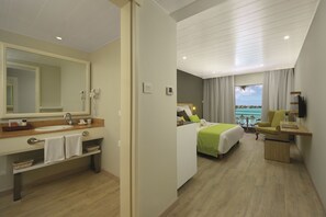 A hotel room with a large mirror, a sink, a bed with green bedding, a chair, and a desk. - Mauricia Beachcomber Resort & Spa (Grand-Baie)
