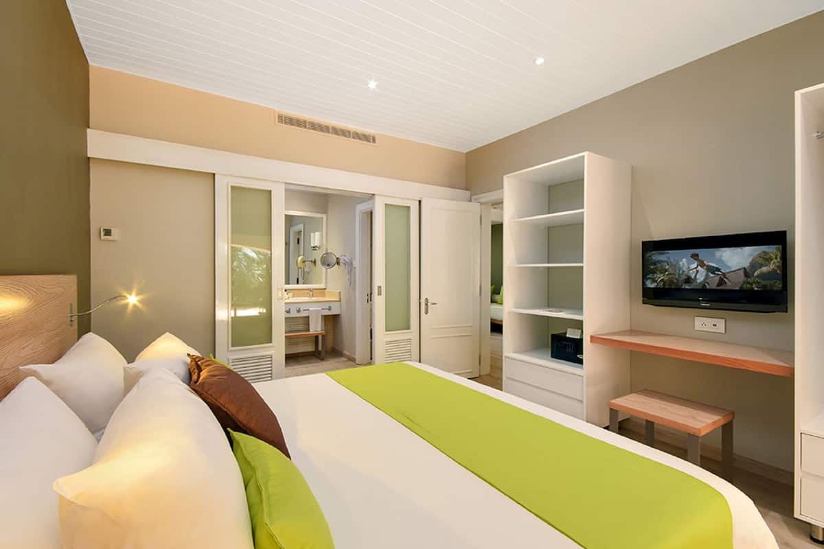 Een moderne hotelkamer met een groot bed, een televisie, een kledingkast en een zichtbare badkamer door een geopende deur.