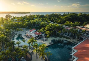 A resort with a large pool surrounded by palm trees, a beach view, and multiple buildings with red roofs. - Mauricia Beachcomber Resort & Spa (Grand-Baie)
