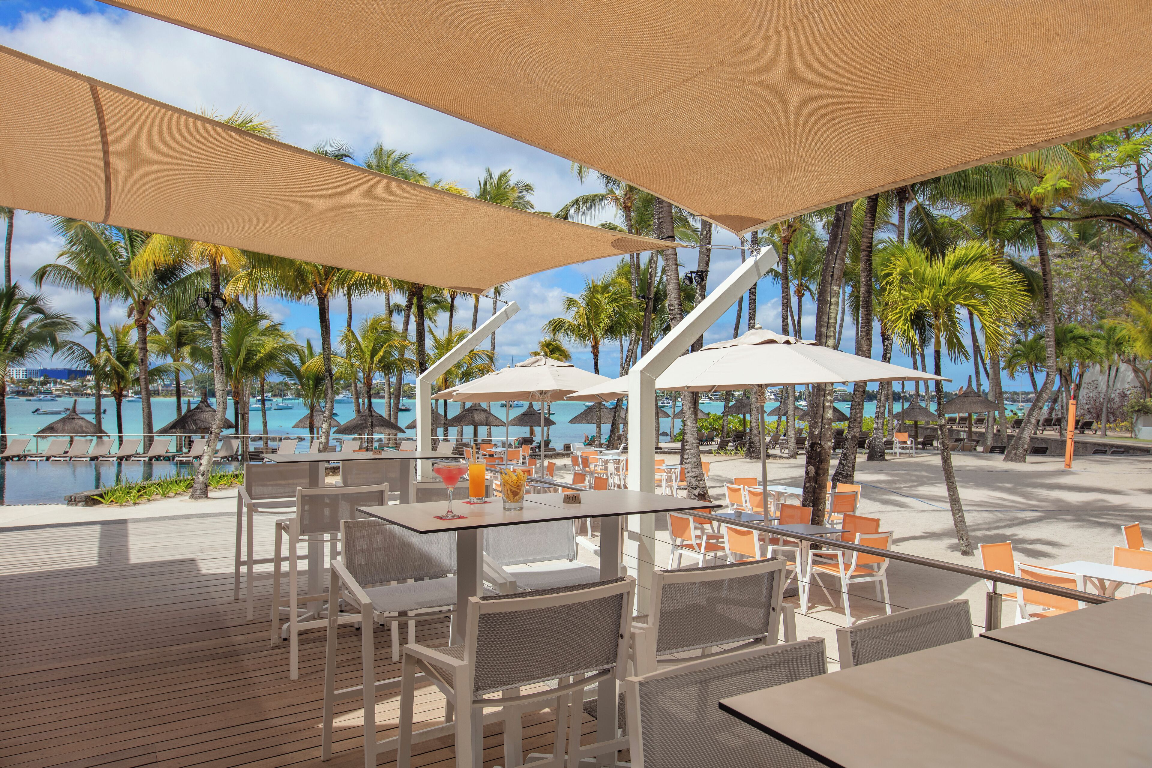 A resort patio with tables and chairs, overlooking a pool and palm trees.