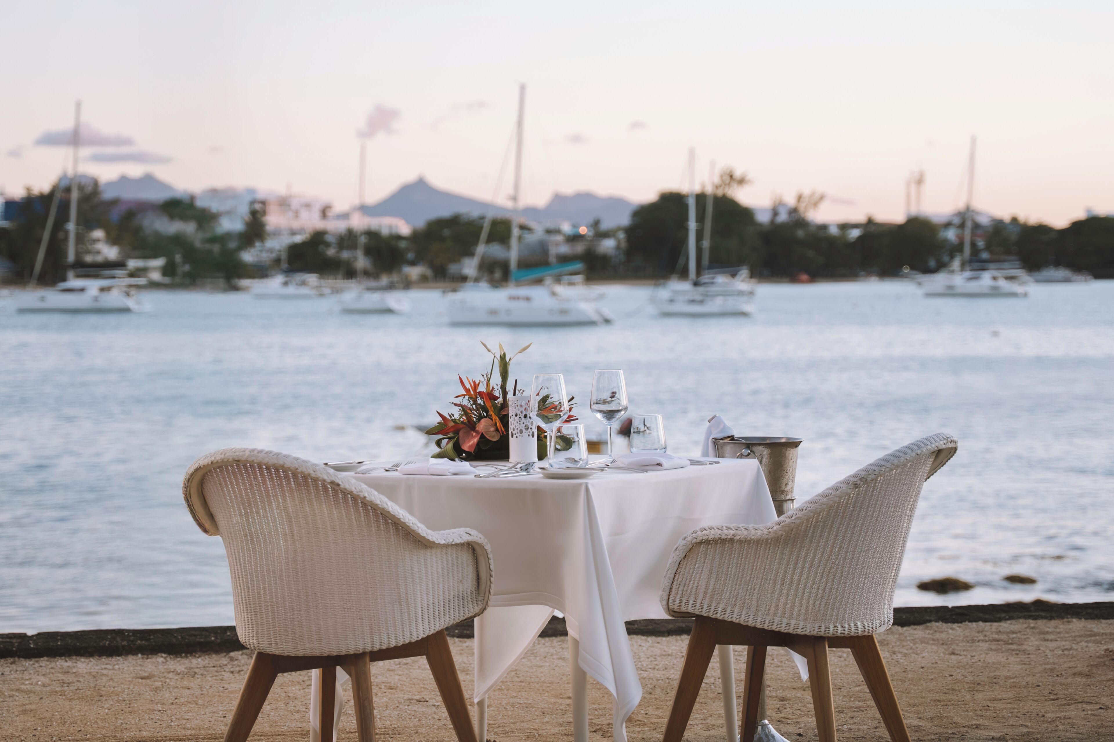A table set for two with a view of the sea and boats in the background.