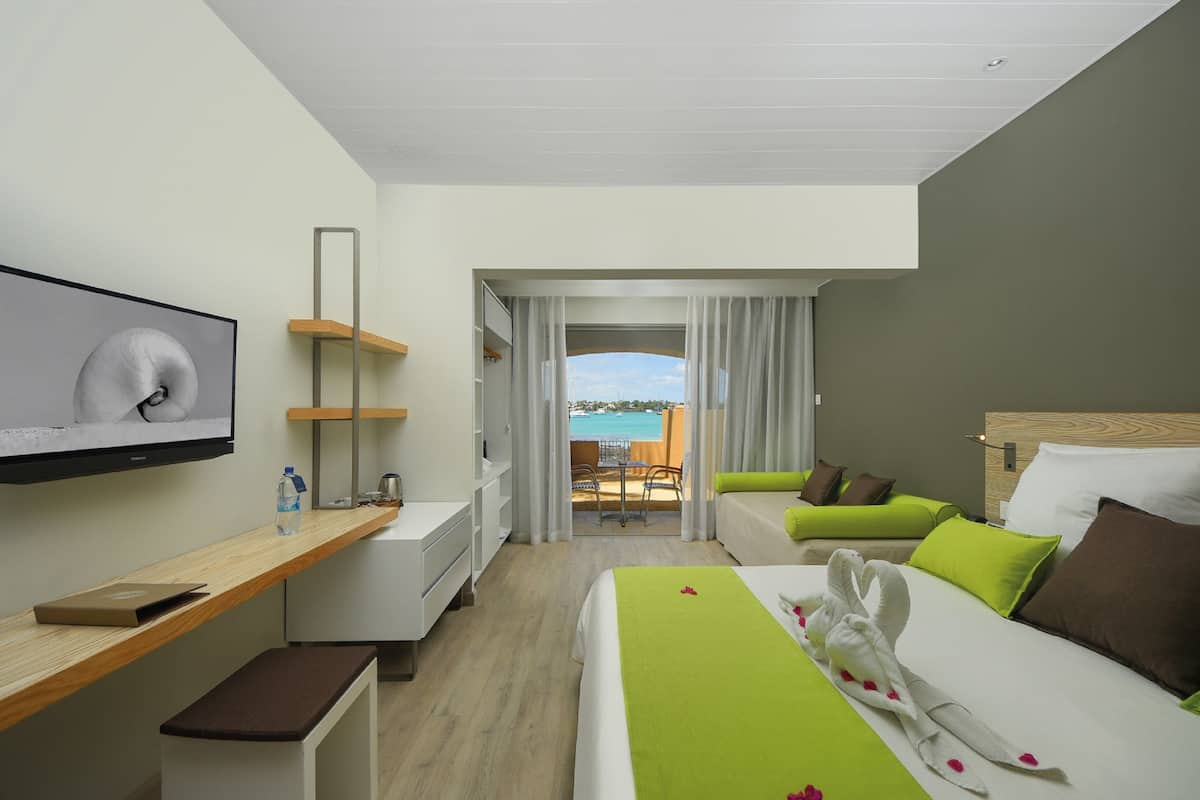 Een hotelkamer met een bed, een bureau, een televisie, een balkon met uitzicht op zee en een schuifdeur naar het balkon.
