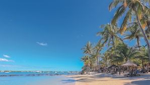 Ein Strand mit klarem, blauem Wasser, Palmen und Hütten mit Strohdächern.