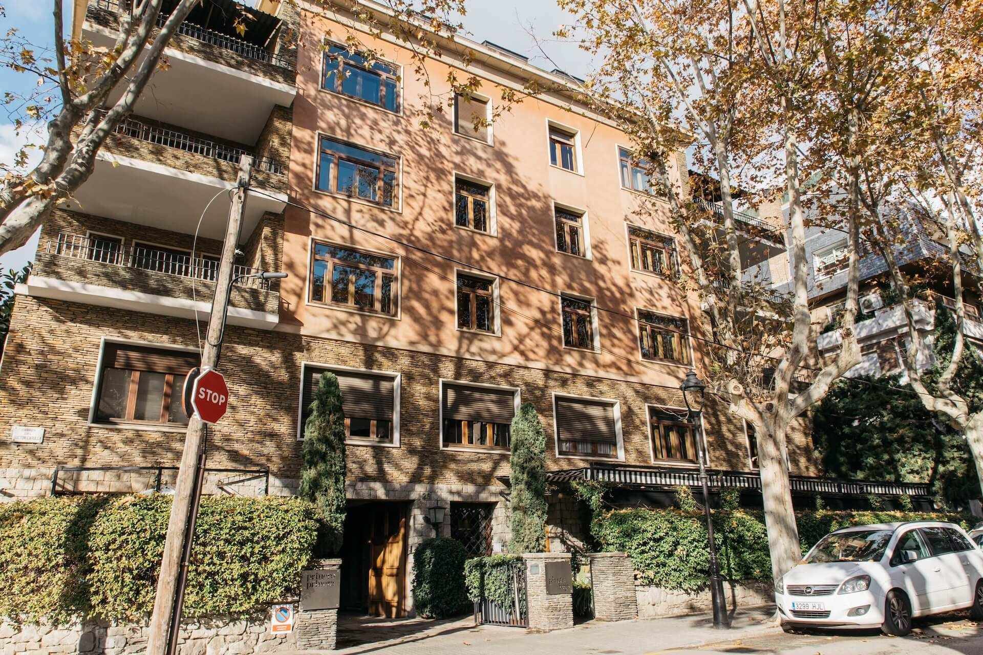 Un edificio de varios pisos con fachada de piedra, una señal de parada y un coche estacionado adelante.