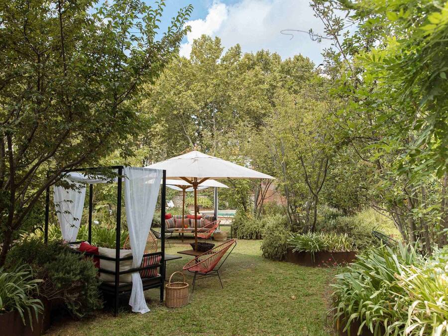 Un jardín con un pabellón, mobiliario exterior y abundante vegetación.