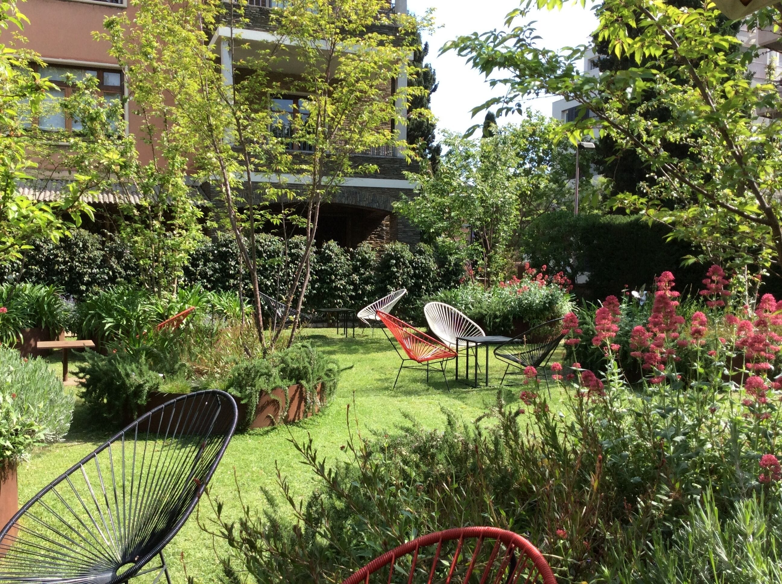 Een verzorgde tuin met diverse zitplekken, waaronder stoelen en een hangmat, omringd door weelderig groen en bloeiende planten.