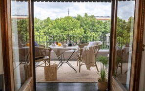 A balcony with wicker furniture, a table set for breakfast, and a view of trees and buildings. - Hotel Primero Primera (Barcelona)