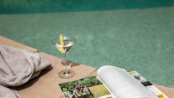 Un magazine, un verre à martini orné d’une tranche de citron et une serviette près d’une piscine.