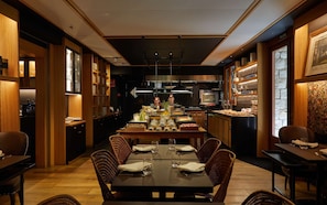 Un restaurante con una larga mesa de comedor, sillas de mimbre y una cocina al fondo.