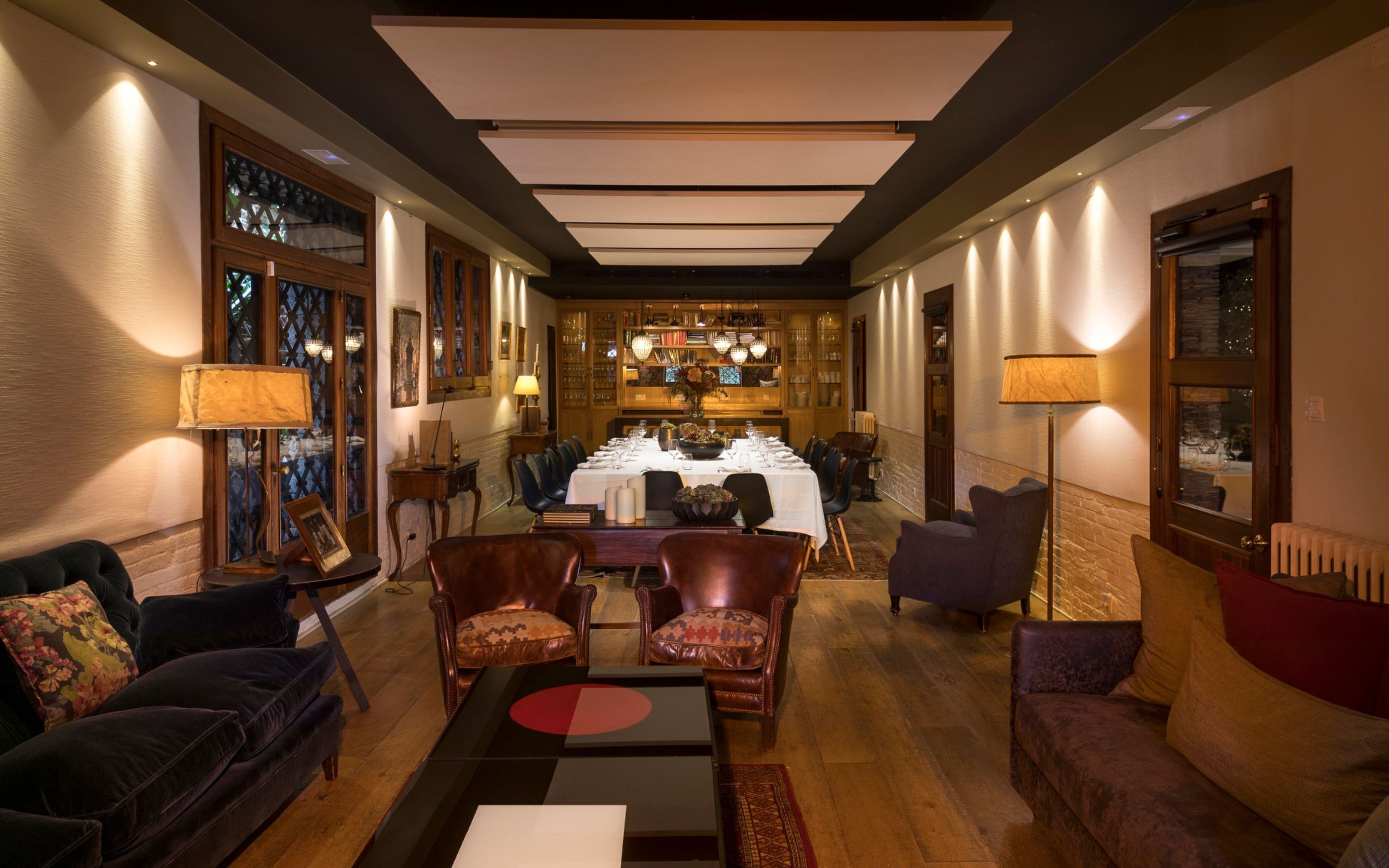 A dining area with a long table set for a meal, surrounded by leather chairs and a sofa.