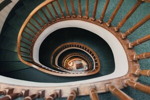 A spiral staircase with wooden balusters and a green carpeted floor.