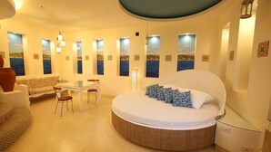 A bedroom with a round bed, a sofa, a dining table, and chairs. There are multiple windows with views of the sea. - Victoria Court Malabon (Malabon)