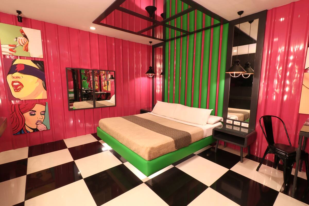 A room with a checkered floor, a bed with green and beige bedding, a red and green striped wall, and a black and white checkered floor.