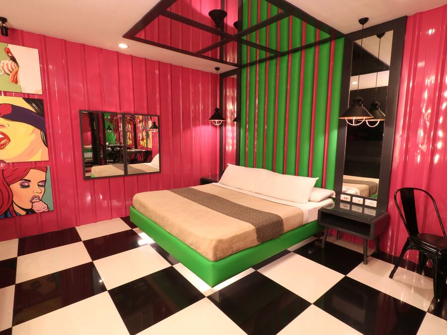 Una habitación con piso a cuadros, cama con ropa de cama verde y beige, pared a rayas rojas y verdes y piso cuadriculado en blanco y negro.