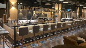 Zona de bar moderna amb una barra llarga, diversos tamborets i una varietat de botelles i gots.