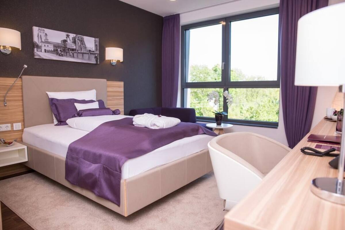 A modern hotel room with a large bed, a desk, a chair, and a bathtub.