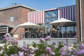 Stylish building with a brick facade and modern glass extension, featuring outdoor seating areas and a metal railing.