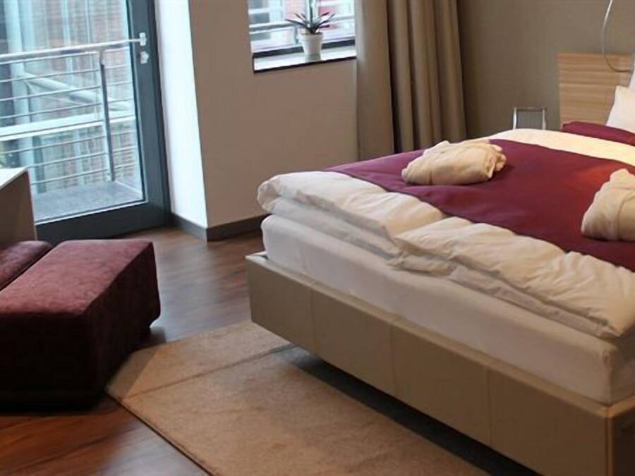 Ein modernes Hotelzimmer mit einem großen Bett, einem Holfnachtkästchen, einem kleinen Tisch und Blick auf die Stadt durch das Fenster.
