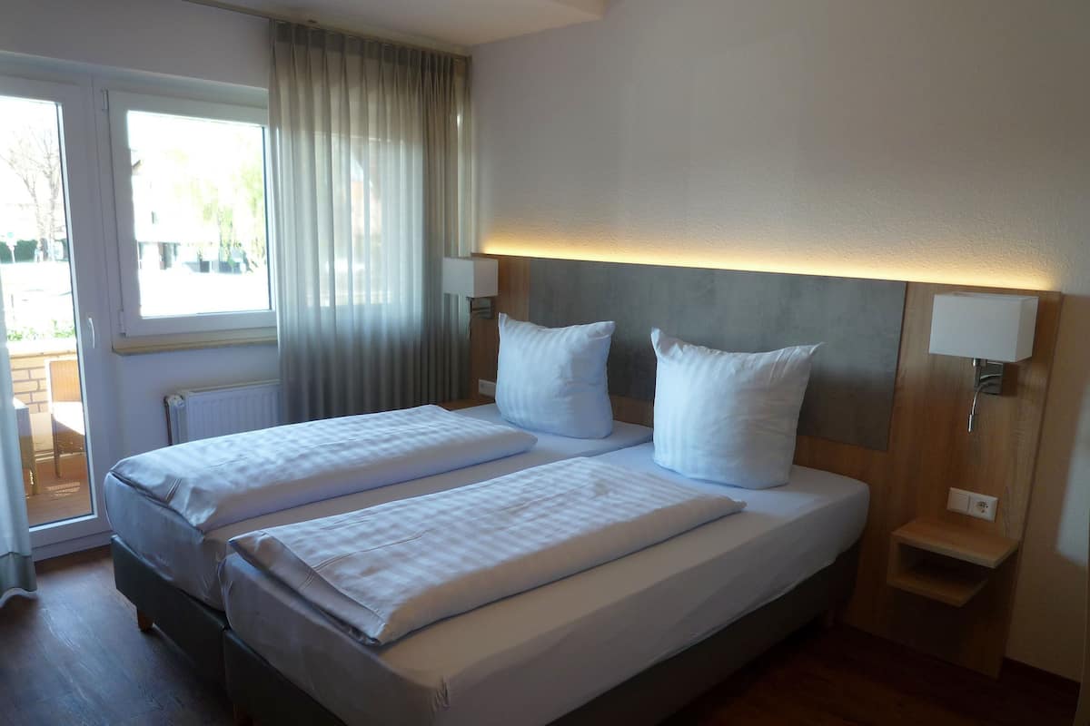 A double bed with white linens, a wooden headboard, and a bedside table with a lamp.