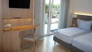 Ein Hotelzimmer mit einem Bett, einem Schreibtisch mit Stuhl, einem an der Wand montierten Fernseher und einer Glastür zu einem Außenbereich.