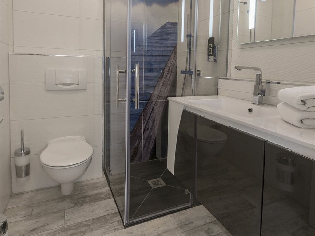 Een moderne badkamer met een douchecabine van glas, een wit toilet en een wastafel met een spiegel erboven.