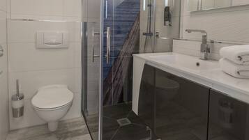 Een moderne badkamer met een douchecabine van glas, een wit toilet en een wastafel met een spiegel erboven.