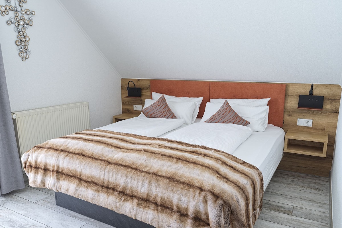 Une chambre d’hôtel moderne avec un grand lit, une tête de lit en bois et une table de chevet avec une lampe.