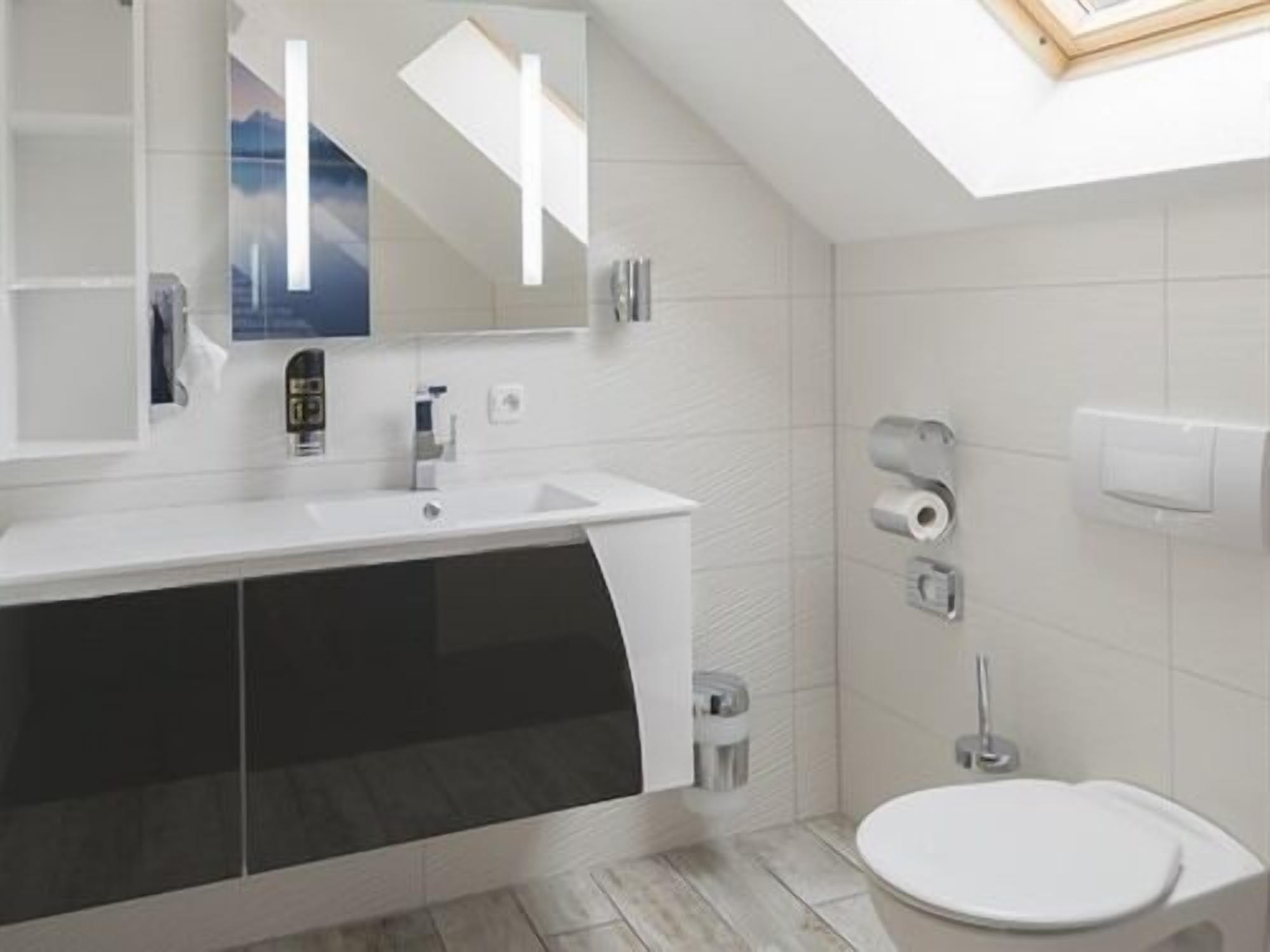 Ein modernes Badezimmer mit Oberlicht, einem großen Spiegel, einem weißen Waschbecken und einer Toilette.