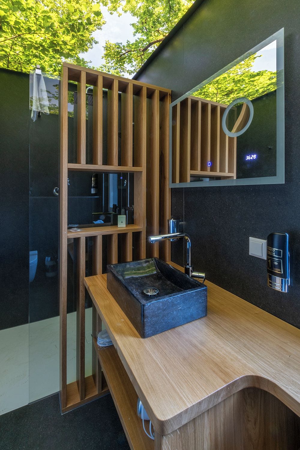 A modern bathroom with a wooden vanity, a black sink, and a mirror.