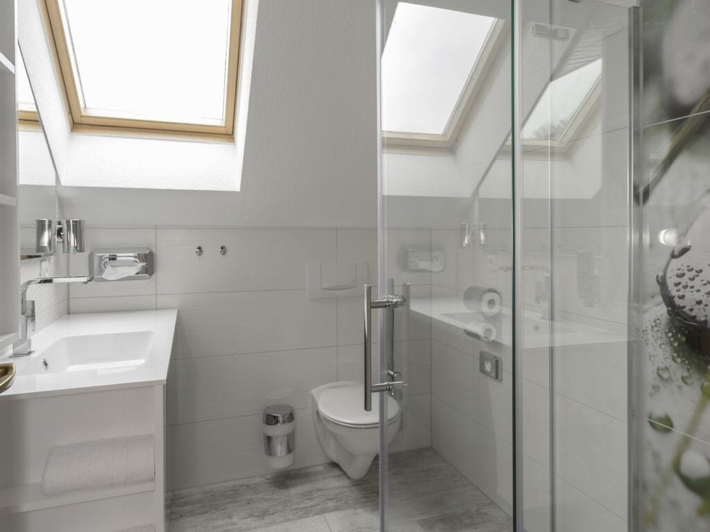 Un baño moderno con tragaluz, cabina de ducha de cristal y lavamanos blanco.