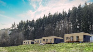 Una hilera de cabañas modernas de madera en un área boscosa, con un campo cubierto de césped en primer plano.